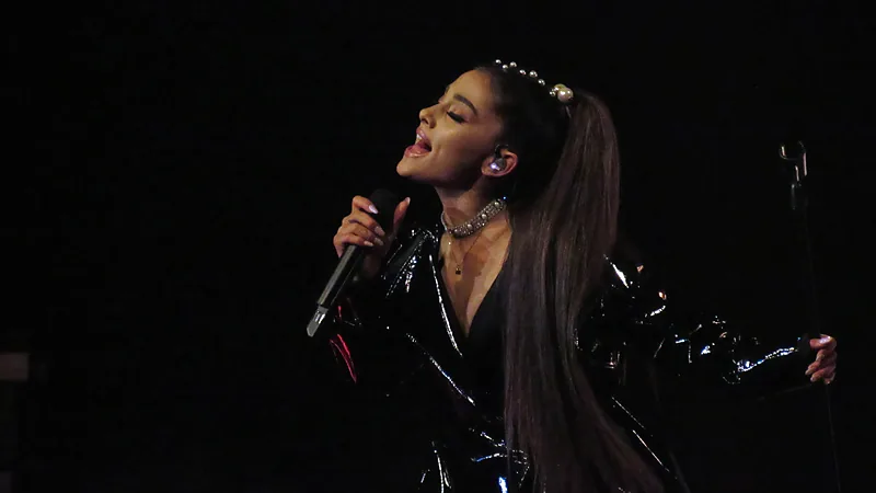 Ariana Grande bernyanyi memegang mikrofon dengan setelan hitam mengilap di atas panggung
