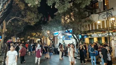 Kerumunan pejalan kaki memadati Jalan Braga Bandung pada malam hari, dengan lampu toko dan pohon di kanan kiri jalan