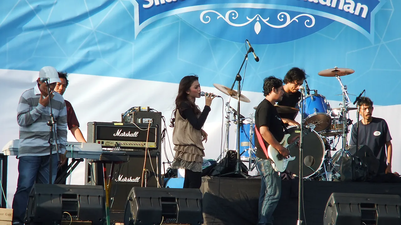 Penyanyi dangdut membawakan lagu di panggung terbuka bersama pemain keyboard, gitar, dan drum