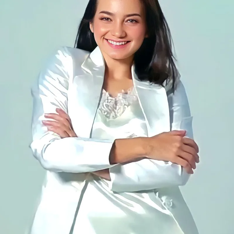 Enzy Storia tersenyum mengenakan blazer putih dengan tangan menyilang di depan dada