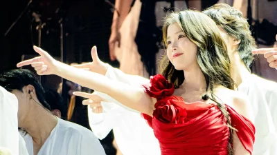 IU bergaun merah menunjuk ke arah penonton di panggung konser HEREH