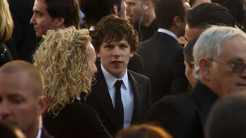Jesse Eisenberg mengenakan setelan hitam di antara kerumunan karpet merah
