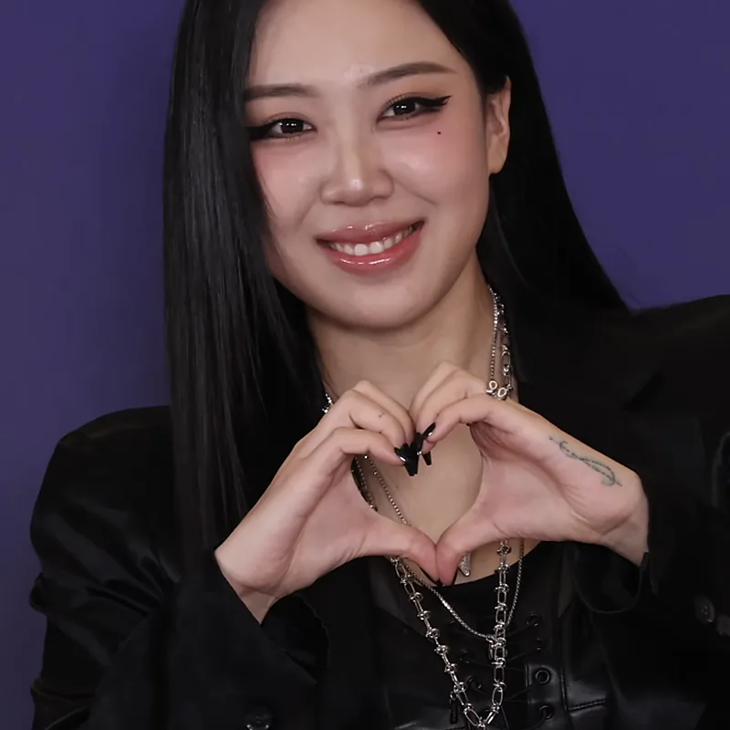 Lee Young-ji tersenyum membentuk tanda hati dengan kedua tangan berlatar ungu