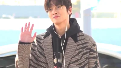 Ji Chang-wook berkacamata melambaikan tangan dengan mantel motif garis di bandara