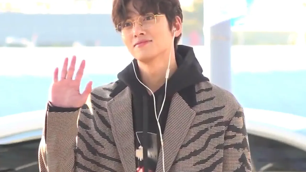 Ji Chang-wook berkacamata melambaikan tangan dengan mantel motif garis di bandara