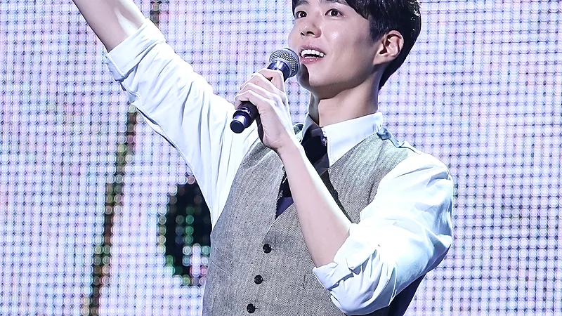 Park Bo-gum bernyanyi memegang mikrofon dan mengangkat tangan di atas panggung