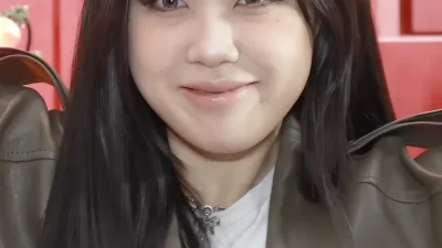 Rapper Lee Young-ji tersenyum berambut hitam panjang mengenakan jaket kulit dengan latar merah
