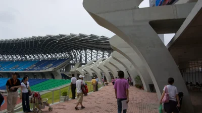 Bagian luar Kaohsiung National Stadium dengan atap baja melengkung dan kursi biru di dalamnya