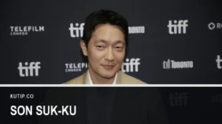 Aktor Son Suk-ku berjas krem di depan dinding sponsor Toronto International Film Festival pada September 2026, dengan nama Son Suk-ku tertulis pada palang di bagian bawah gambar