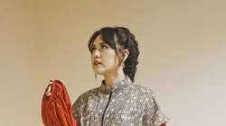 Potret penyanyi Happy Asmara mengenakan busana bermotif sambil memegang kain merah