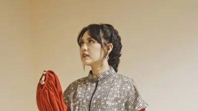 Potret penyanyi Happy Asmara mengenakan busana bermotif sambil memegang kain merah