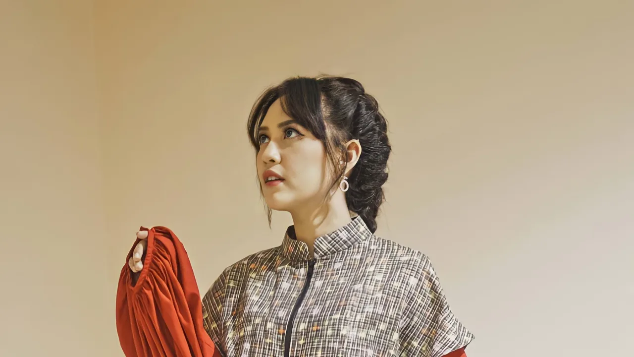 Potret penyanyi Happy Asmara mengenakan busana bermotif sambil memegang kain merah