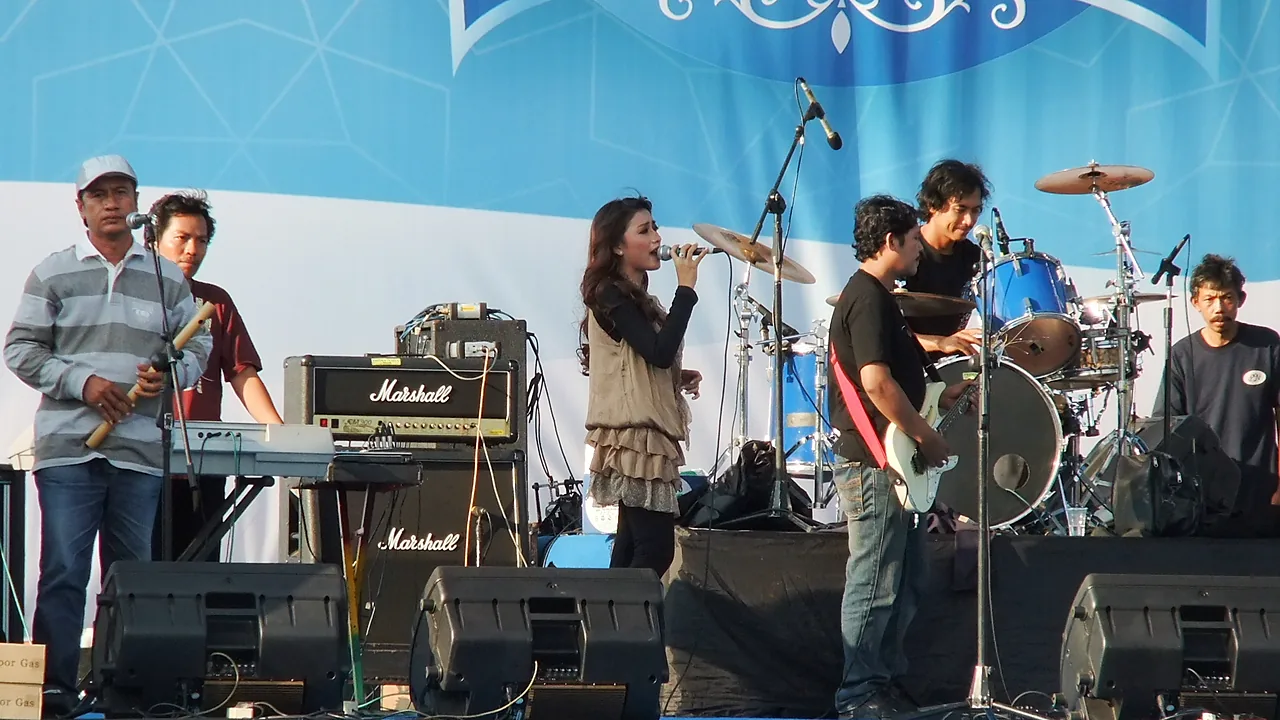 Penyanyi dangdut perempuan membawakan lagu di panggung terbuka bersama pemain keyboard, gitar, dan drum