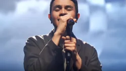 Penyanyi Tulus memejamkan mata sambil menggenggam mikrofon di atas panggung