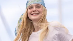 Elle Fanning tersenyum mengenakan ikat kepala bermotif bunga di acara luar ruang, dengan teks Sunrise on the Reaping