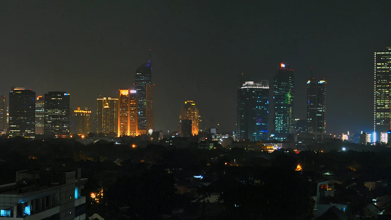 Panorama malam Jakarta dengan gedung-gedung tinggi menyala di kejauhan