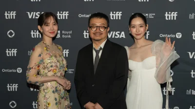 Sutradara Yeon Sang-ho berdiri di antara dua pemeran perempuan di depan dinding Toronto International Film Festival