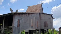 Rumah adat Banjar Bubungan Tinggi berdinding kayu tua dengan atap tinggi, berdiri di atas tiang