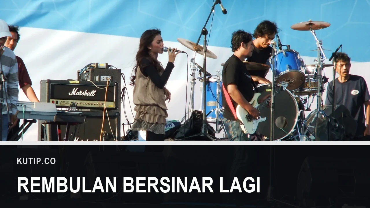 Penyanyi dangdut perempuan bernyanyi memegang mikrofon di panggung terbuka bersama pemain gitar, drum, dan keyboard, dengan tulisan Rembulan Bersinar Lagi pada palang di bagian bawah gambar